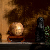 HEART SUTRA GOLD GLOBE glowing warmly on wood base, refined centerpiece blending spiritual symbolism with contemporary elegance.