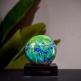 Van Gogh Irises MOVA Globe, displayed with greenery background, sophisticated rotating art piece for stylish home décor.
