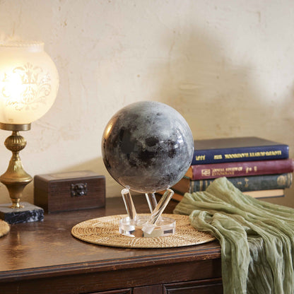 Moon MOVA Globe displayed on wooden desk with books and lamp